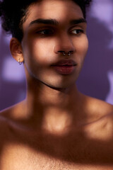 Wall Mural - Verticale portrait of sensual young man in shadows. Sensitive hispanic model on purple background