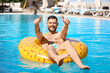 © Pixel-Shot - Young man with inflatable ring showing thumbs-up in swimming pool