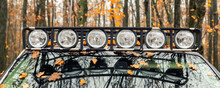 Close-up Detail View Of Custom Made Roof Rack Bar With Extra Headlight Mounted On Roof Of Heavy Duty Pick Up Suv Car Against Foggy Autumn Forest. Fallen Leaves Vehicle Windshield. Fall Weather Drive
