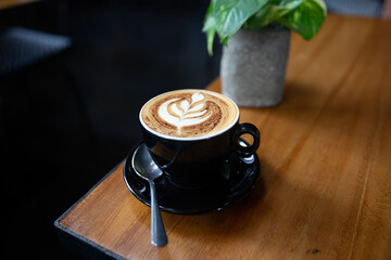 Cup of tasty cappuccino with latte art on wooden table background.