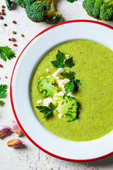 Poster - Broccoli soup puree in plate on gray tile background with ingredients. Cooking healthy food concept.