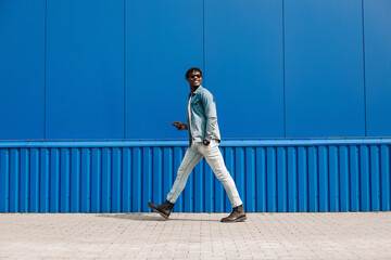 african guy walks with a phone around the city, against the background of a blue building, makes a purchase online