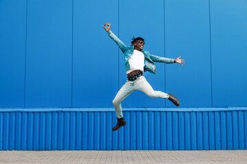 african guy jumping with a phone in his hands, in the city against the background of a blue building