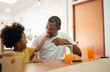 © eggeeggjiew - African American Father and little son eating Croissant and drinking juice for breakfast in dining room