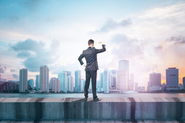 Poster - Back view of young man standing on concrete edge of building on city background with mock up place in sky. Success, future, vision and leadership concept.
