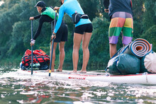 Three Teenage Tourists Row Down The River In A Large Inflatable SUP. Water Tourism And Active Lifestyle Concept