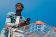 Afro black man with a shopping cart and a phone in his hands, makes purchases online, background blue