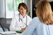 © sepy - Female doctor consulting her patient while sitting at desk in doctor's office