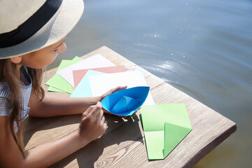 Poster - Little girl making paper boats on wooden pier near river