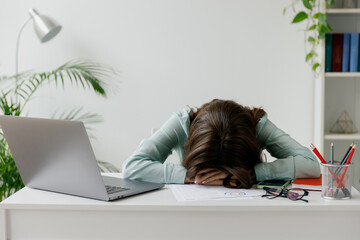 Young sleepy frustrated employee business woman 20s in blue shirt put head down on table sit work at workplace white desk with laptop pc computer at light office indoors. Achievement career concept