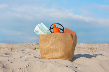 Beach bag with towel, book and sunscreen on sand