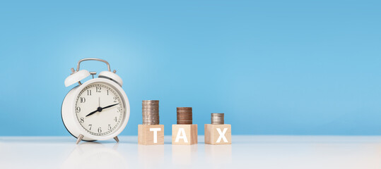 white word tax on wooden cube with stack coins and alarm clock on table blue background. economy investment wealth. Tax finance business concept.