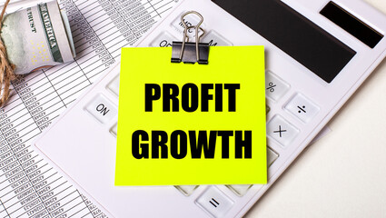 Fototapete - On a light background - cash, a white calculator and a yellow sticker under a black paper clip with the text PROFIT GROWTH. Business concept