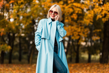 Happy beautiful young happy business woman with a smile in fashionable elegant clothes talking on the phone in the autumn golden park