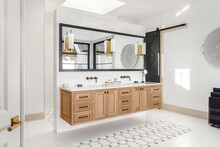 Bathroom in luxury home with double vanity. Features floating hardwood cabinets and faucets, large mirror, and elegant tile floor.  A skylight allows for abundant natural light.