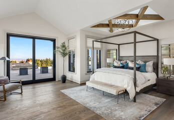 Bedroom in new luxury home with hardwood floors, sliding glass door leading to patio, and skylights with wood cross beams and elegant pendant light