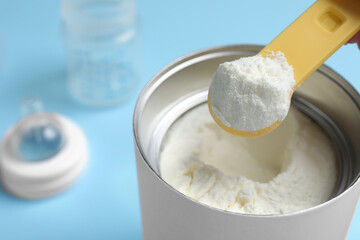 Wall Mural - Scoop of powdered infant formula over can on light blue background, closeup. Baby milk