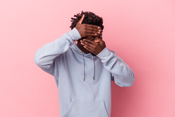 Wall Mural - Young african american man isolated on pink background blink at the camera through fingers, embarrassed covering face.