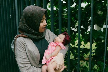 Wall Mural - Happy asian mom holding her little baby daughter wearing hijab