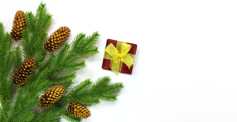 Fir branches with cones in corner and red gift box with yellow bow on white background. Christmas, New Year. Copy space