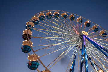 Wall Mural - Low angle view of colourful illuminating Ferris wheel at carnival amusement park, against beautiful twilight sky.