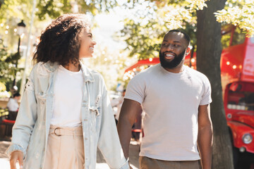 Cheerful young african couple walking together on romantic date outdoors in city park. Love and relationship, bonding concept