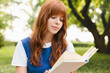 © InsideCreativeHouse - Young red-haired red-head woman teenage girl with ginger hair reading book outdoors in park. Teenager schoolgirl doing homework, preparing for exam sitting on the grass.
