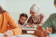 © Minet - Female hijab muslim teacher helps school kids to finish they lesson. Selective focus