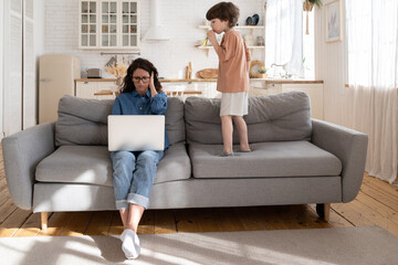 Wall Mural - Mother working from home cover ears with hands to protect from loud noises from hyperactive preschool child try to focus on laptop computer on covid-19 lockdown school closed and remote work lifestyle