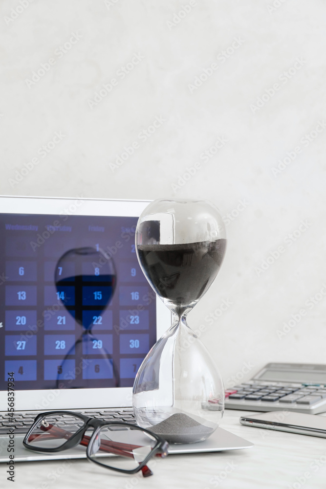 Hourglass, eyeglasses and laptop with calendar on light background. Deadline concept