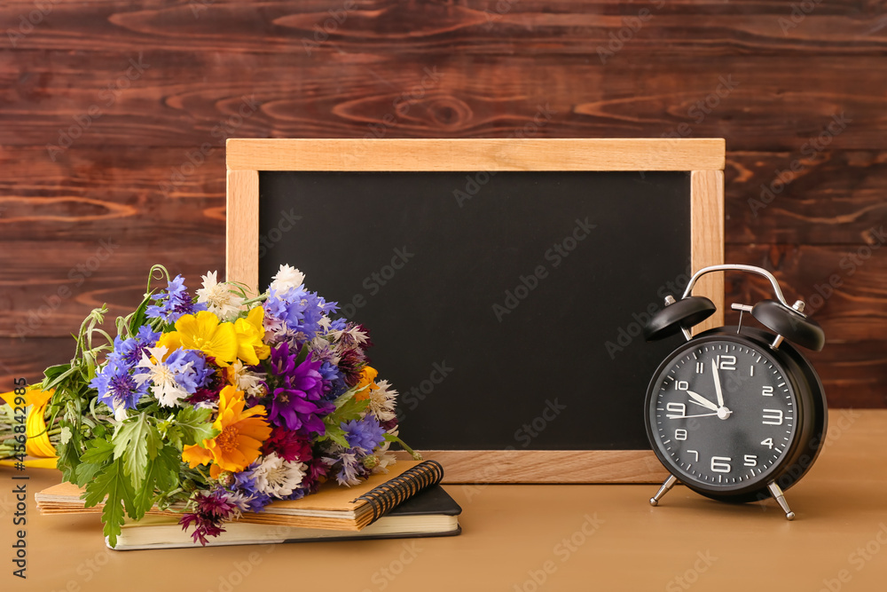Blank chalkboard, alarm clock and beautiful flowers on wooden table