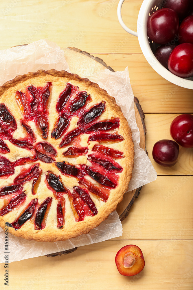 Board with tasty plum pie on wooden background