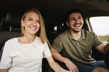 Wall Mural - Beautiful young couple sitting on front passenger seats and driving a car