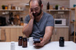 © DC Studio - Caucasian man with headache looking at smartphone holding bottle of pills for pain remedy, treatment, medication, medicine. Adult with migraine having container with medical drugs