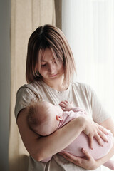 Wall Mural - Contemporary young woman cradling adorable baby daughter while holding her on hands