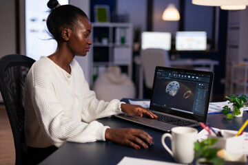 Wall Mural - Focused african american engineer woman working at industrial gear prototype late at night in startup business company office. Engineering product construction idea on laptop screen