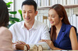 © butsaya33 - Young Asian couple talking about house investment financial plan with house sale agency. The customer and the employee are discussing the materials by looking at the materials. Real estate concept