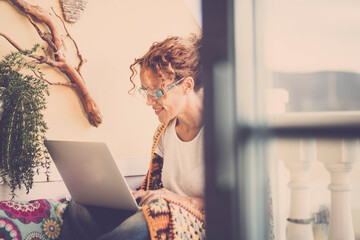 Young woman using laptop and working while sitting on terrace. Pleased woman working or studying on laptop at house terrace. Happy young female browsing internet or social media apps on laptop