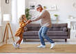 Active senior grandfather enjoying dance with cute little granddaughter in living room at home