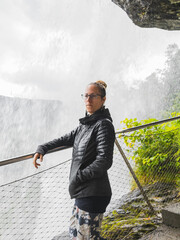 Poster - Middle-aged Caucasian woman wearing glasses leaning on a bridge in front of the waterfall