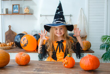 A Little Girl In A Witch Costume At Home In The Kitchen With Pumpkins For Halloween