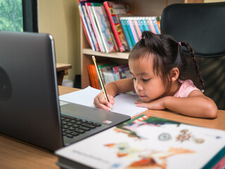 Cute little schoolgirl studying homework math during her online lesson at home, social distancing during the coronavirus outbreak. Concept of online education or home schooler.