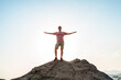 © KseniaJoyg - A happy young man with his hands raised stands on a picturesque steep cliff above the sea against the sky. The concept of travel and freedom.
