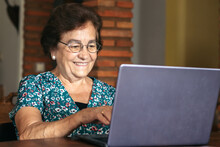 Smiling Senior Woman Typing On Laptop In Room