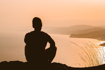 Wall Mural - Silhouette of a man at sunset on a cliff with a magnificent landscape and a view of the sea and mountains