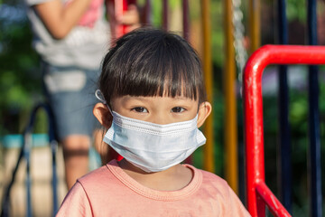 Wall Mural - Portrait image of 3-4 yeas old baby. Happy Asian child girl wearing fabric mask,​ at the park playground, social​ Distance,​ Learning and active of kids concept.