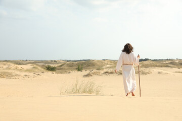 Wall Mural - Jesus Christ walking with stick in desert, back view. Space for text