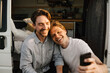© Maskot - Smiling male friends taking selfie on mobile phone at doorway of camping van