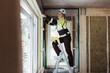 © Maskot - Full length of female building contractor measuring window frame standing on step ladder at construction site