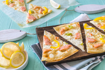 Wall Mural - Pieces of tarte flambee with salmon, yellow pepper and spring onions on a wooden board on light green background